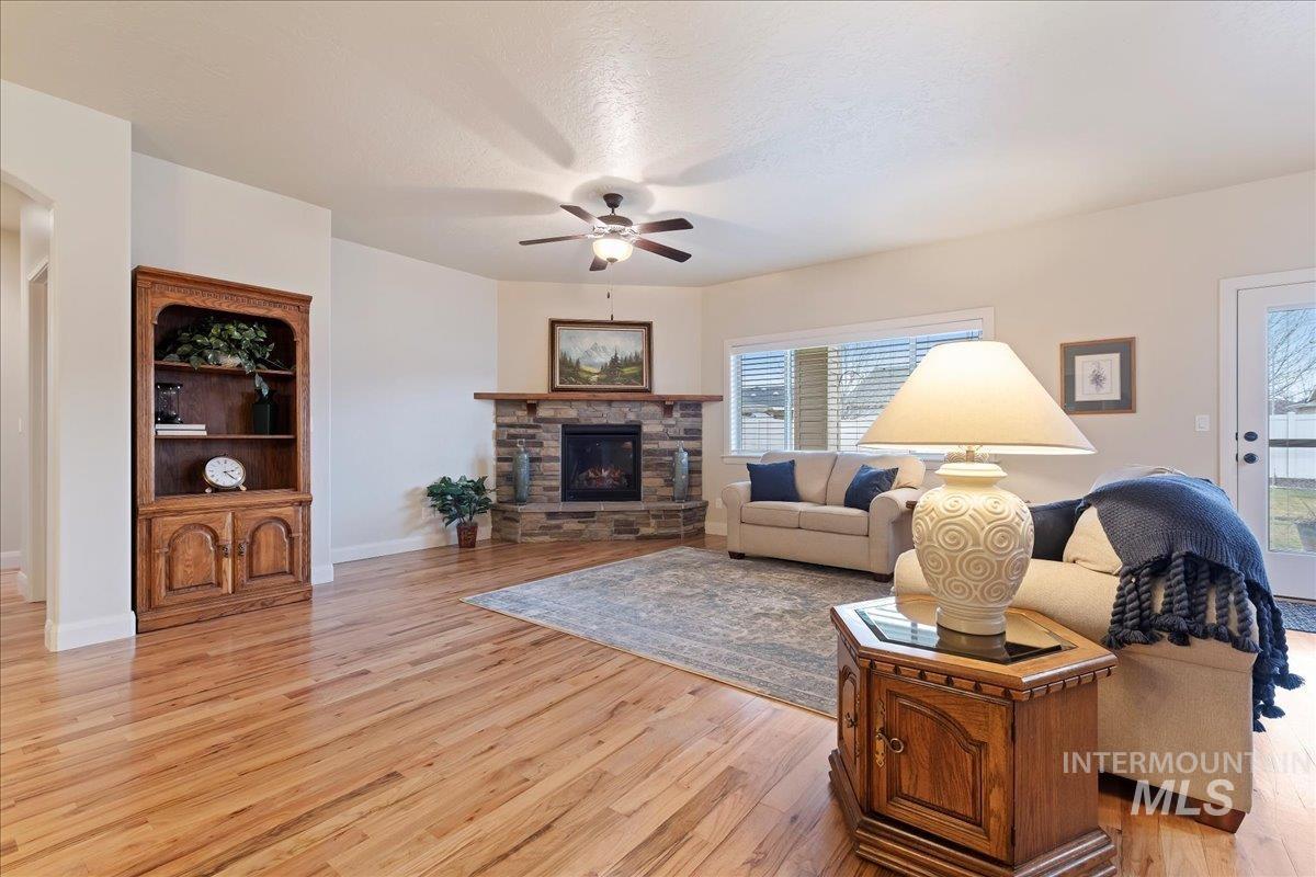 Living room with a stone fireplace, light wood-style flooring, ceiling fan, and a textured ceiling