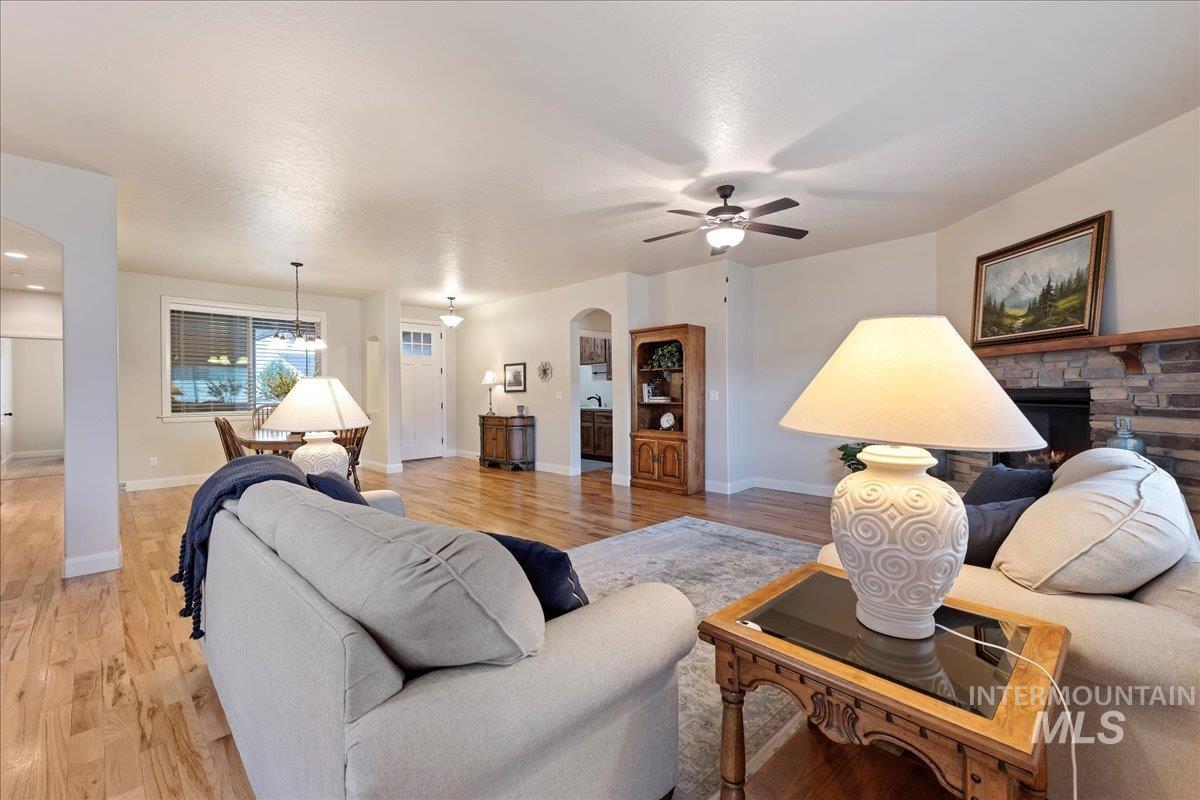 Living area with arched walkways, light wood-style flooring, a stone fireplace, and a ceiling fan
