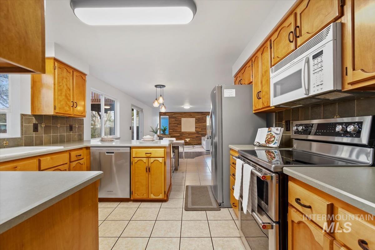 Kitchen featuring appliances with stainless steel finishes, light countertops, brown cabinets, and hanging light fixtures