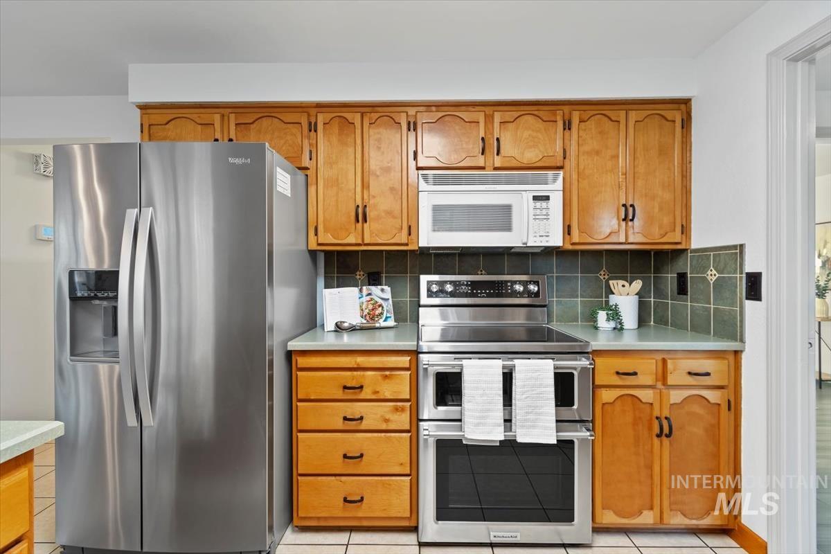 Kitchen featuring appliances with stainless steel finishes, light countertops, decorative backsplash, and brown cabinets