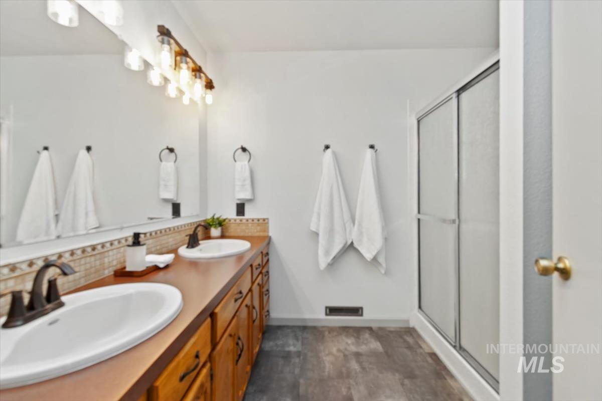 Bathroom with double vanity, a shower stall, and decorative backsplash