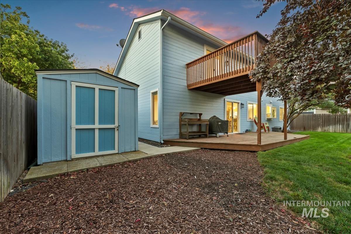Back of property at dusk featuring a fenced backyard, a wooden deck, and a storage shed