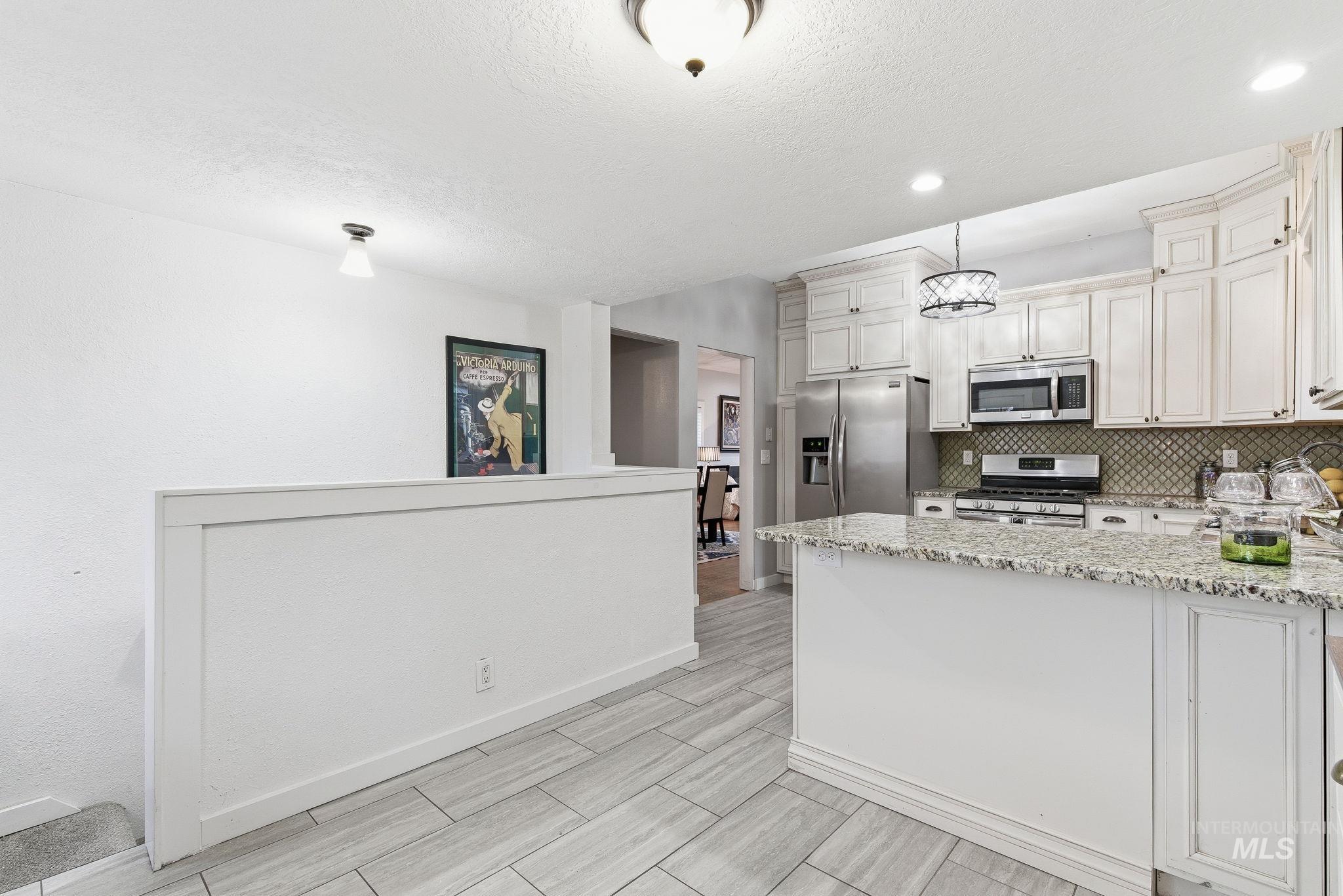 Kitchen with light stone counters, appliances with stainless steel finishes, tasteful backsplash, a textured ceiling, and a peninsula