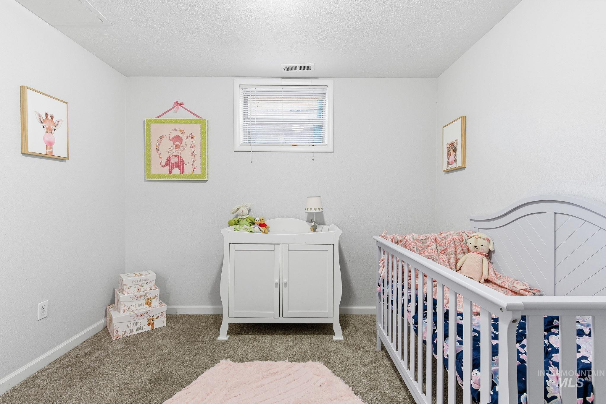 Carpeted bedroom with a textured ceiling and a nursery area