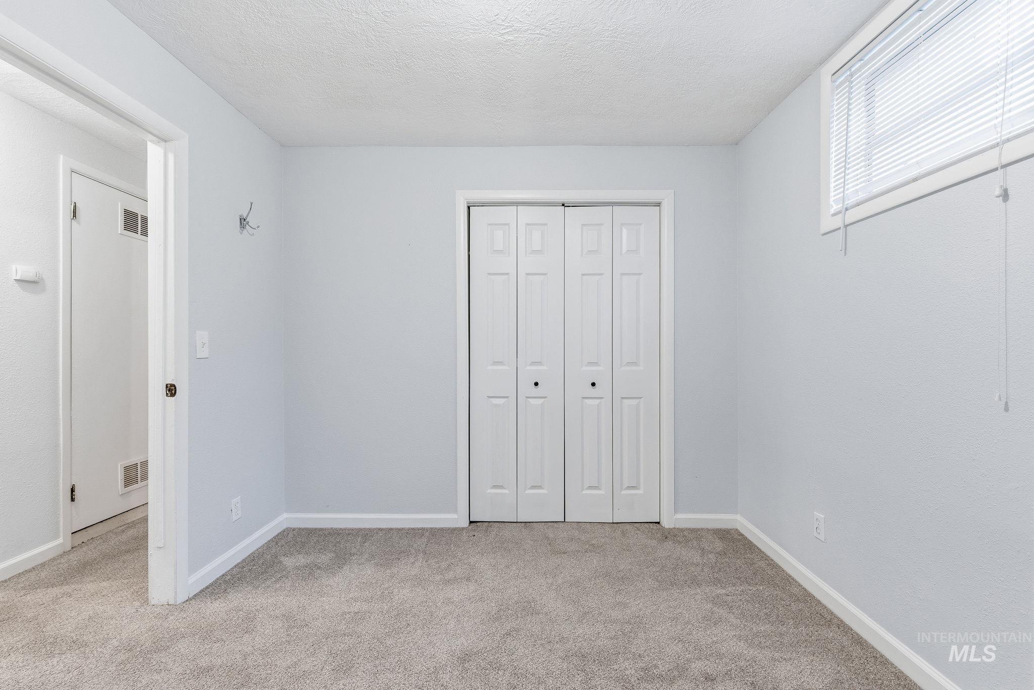 Unfurnished bedroom featuring a textured ceiling, light carpet, and a closet