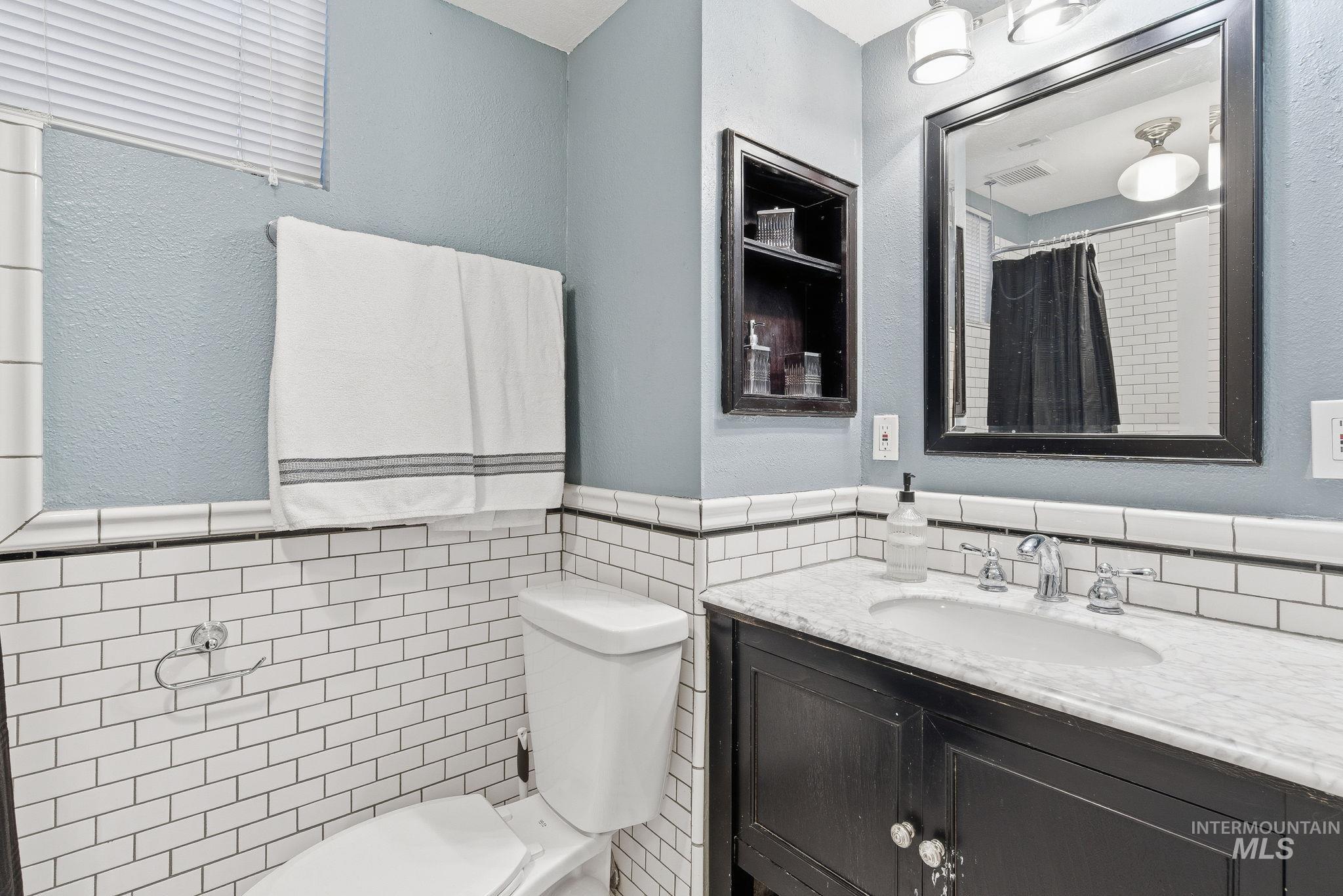 Full bathroom with vanity, a textured wall, curtained shower, tile walls, and a wainscoted wall