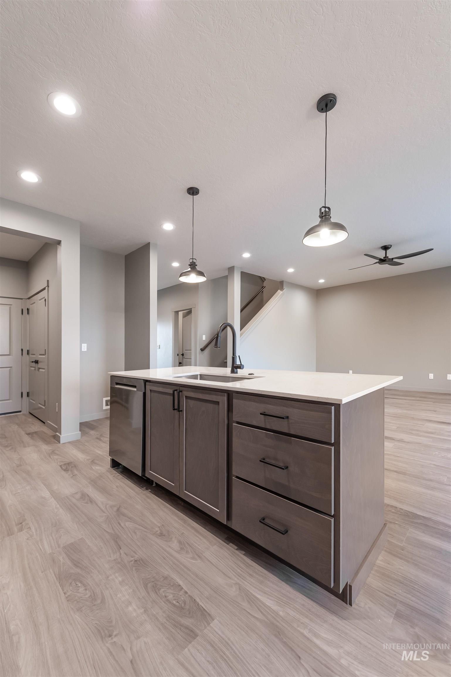 Kitchen with hanging light fixtures, an island with sink, open floor plan, light wood-style floors, and recessed lighting