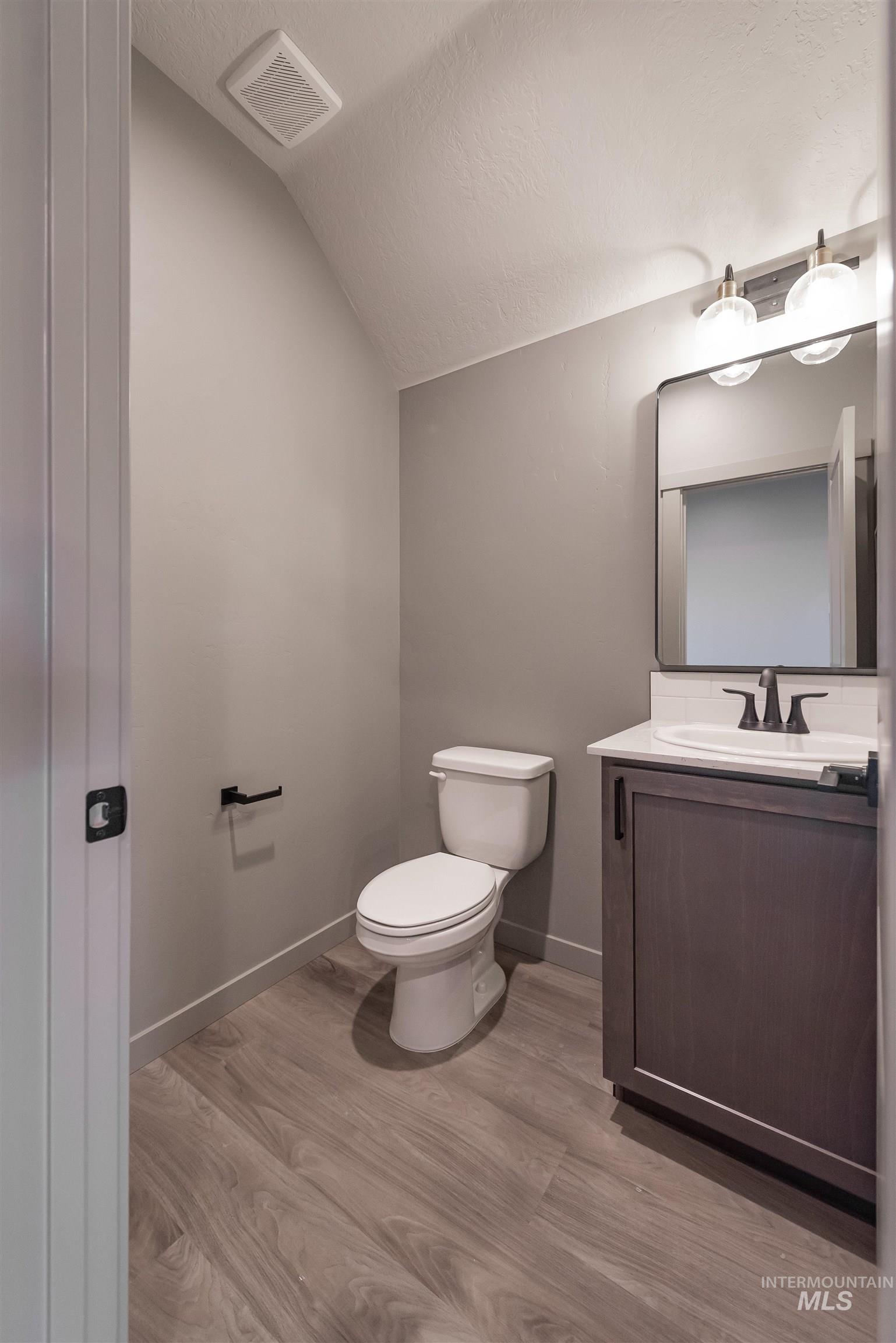 Bathroom with vanity, vaulted ceiling, light wood finished floors, and a textured ceiling
