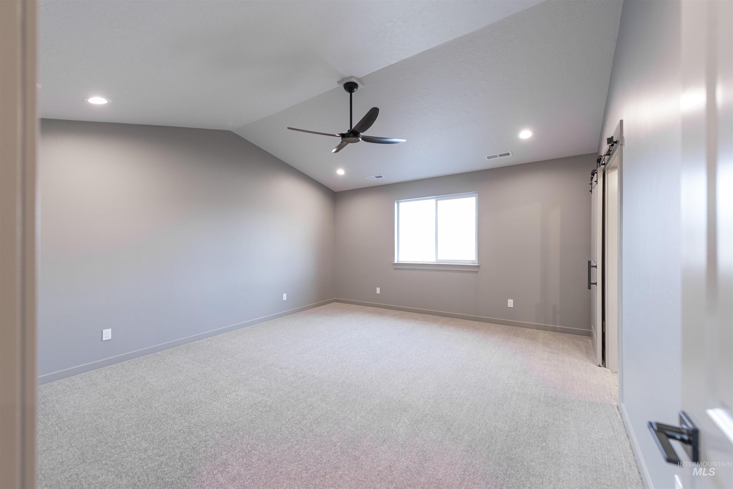 Empty room featuring a barn door, vaulted ceiling, light colored carpet, recessed lighting, and ceiling fan