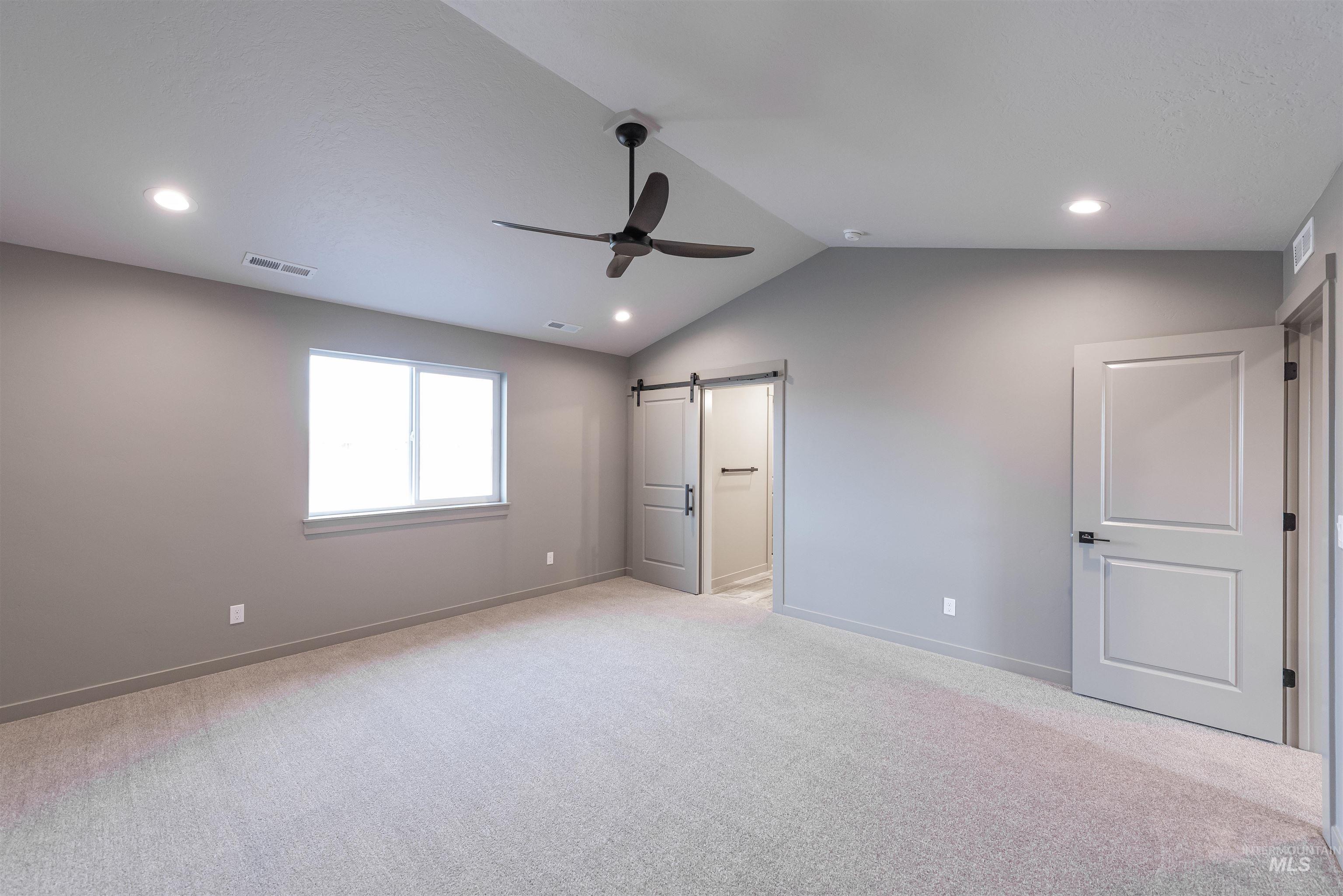 Unfurnished bedroom featuring a barn door, lofted ceiling, light carpet, a ceiling fan, and recessed lighting