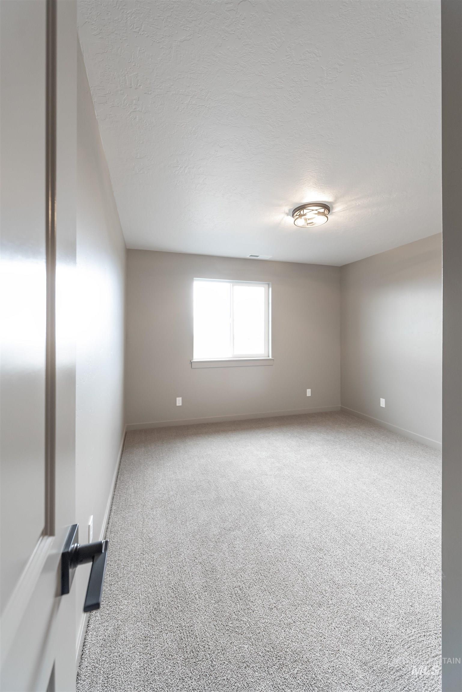 Carpeted empty room with a textured ceiling and baseboards