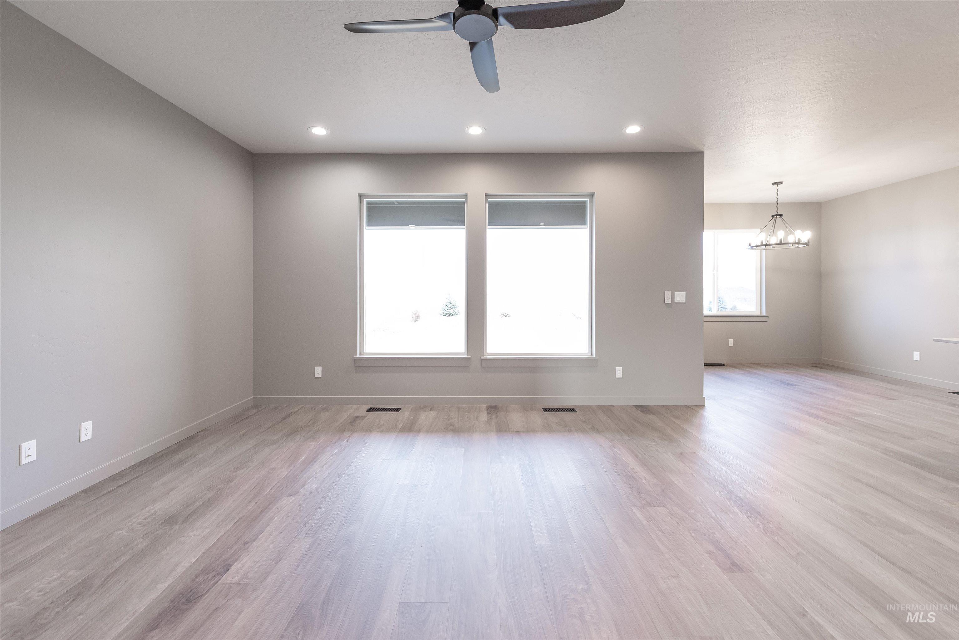 Spare room featuring a ceiling fan, light wood-type flooring, a chandelier, and recessed lighting