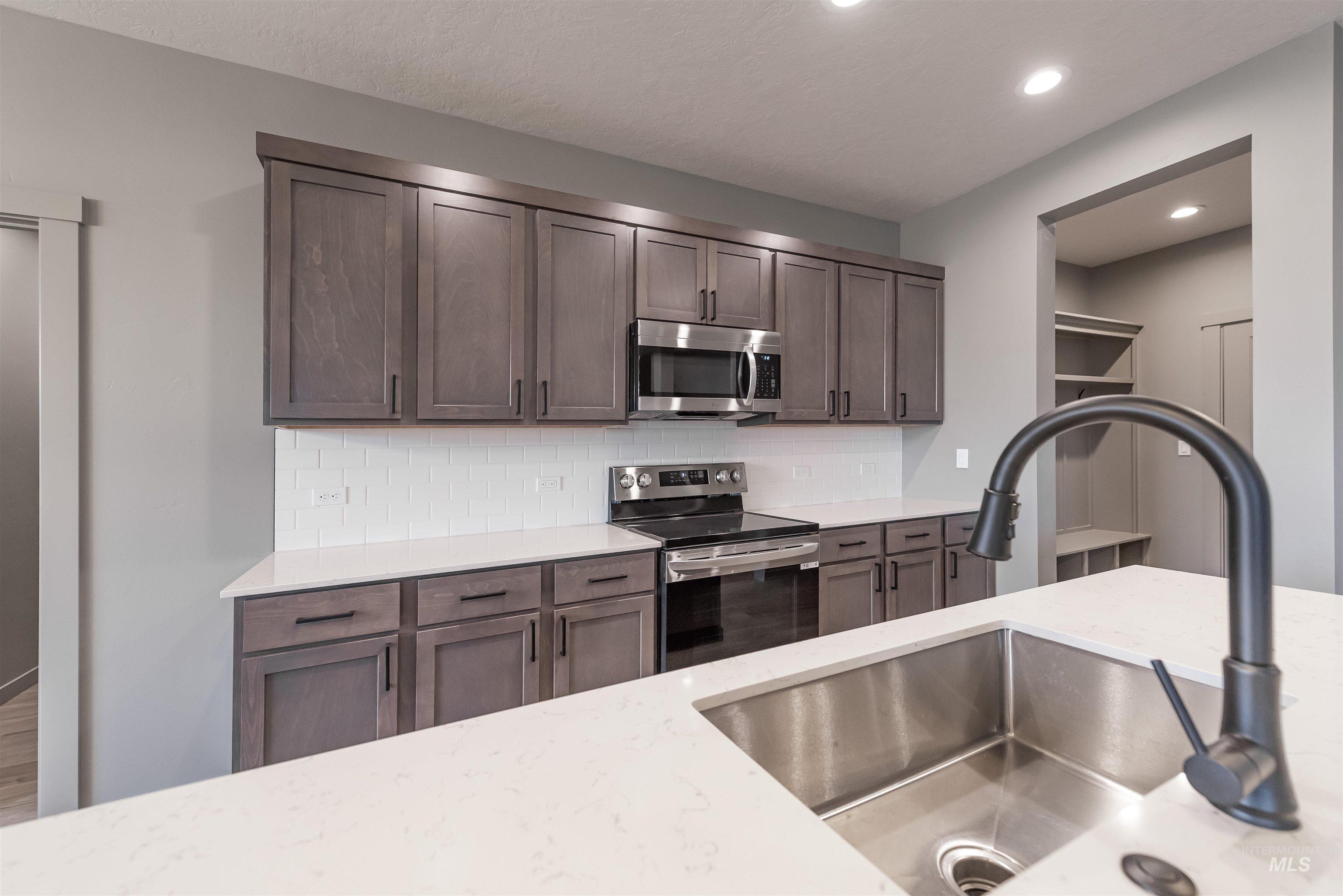 Kitchen with stainless steel appliances, backsplash, light stone countertops, dark brown cabinets, and recessed lighting