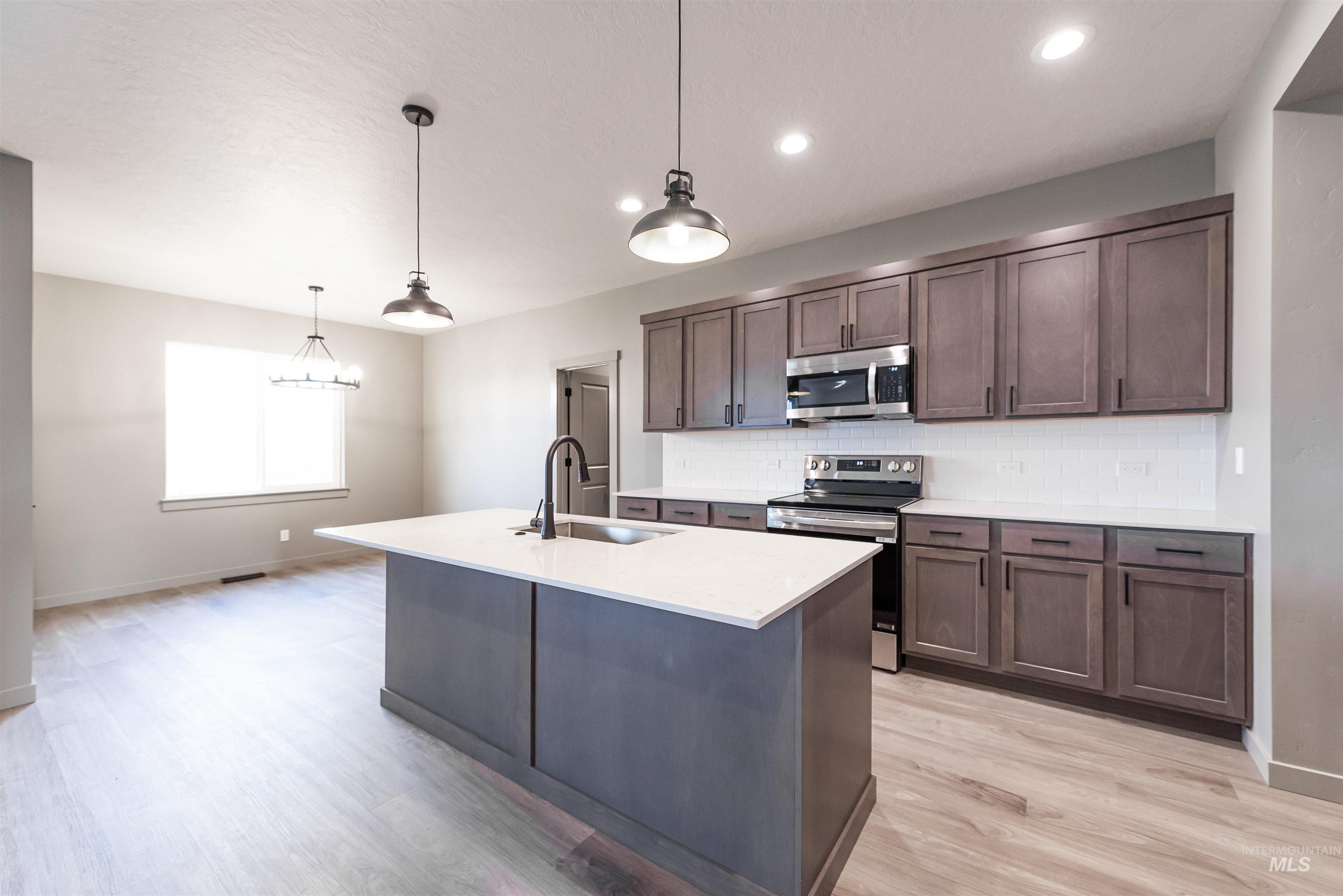 Kitchen featuring stainless steel appliances, pendant lighting, a center island with sink, backsplash, and light wood-style flooring