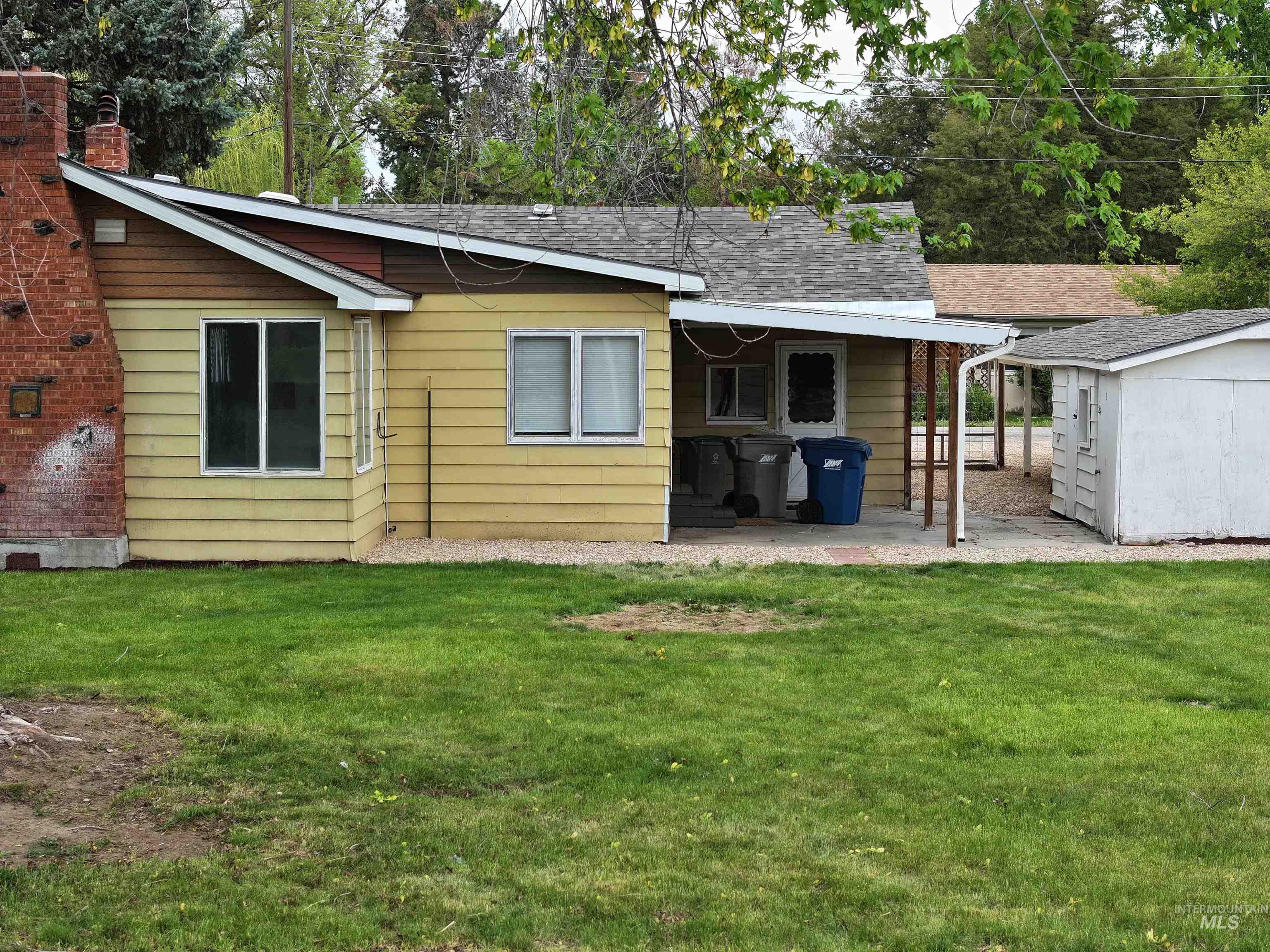 Rear view of house with a lawn, a shingled roof, a chimney, a shed, and a patio