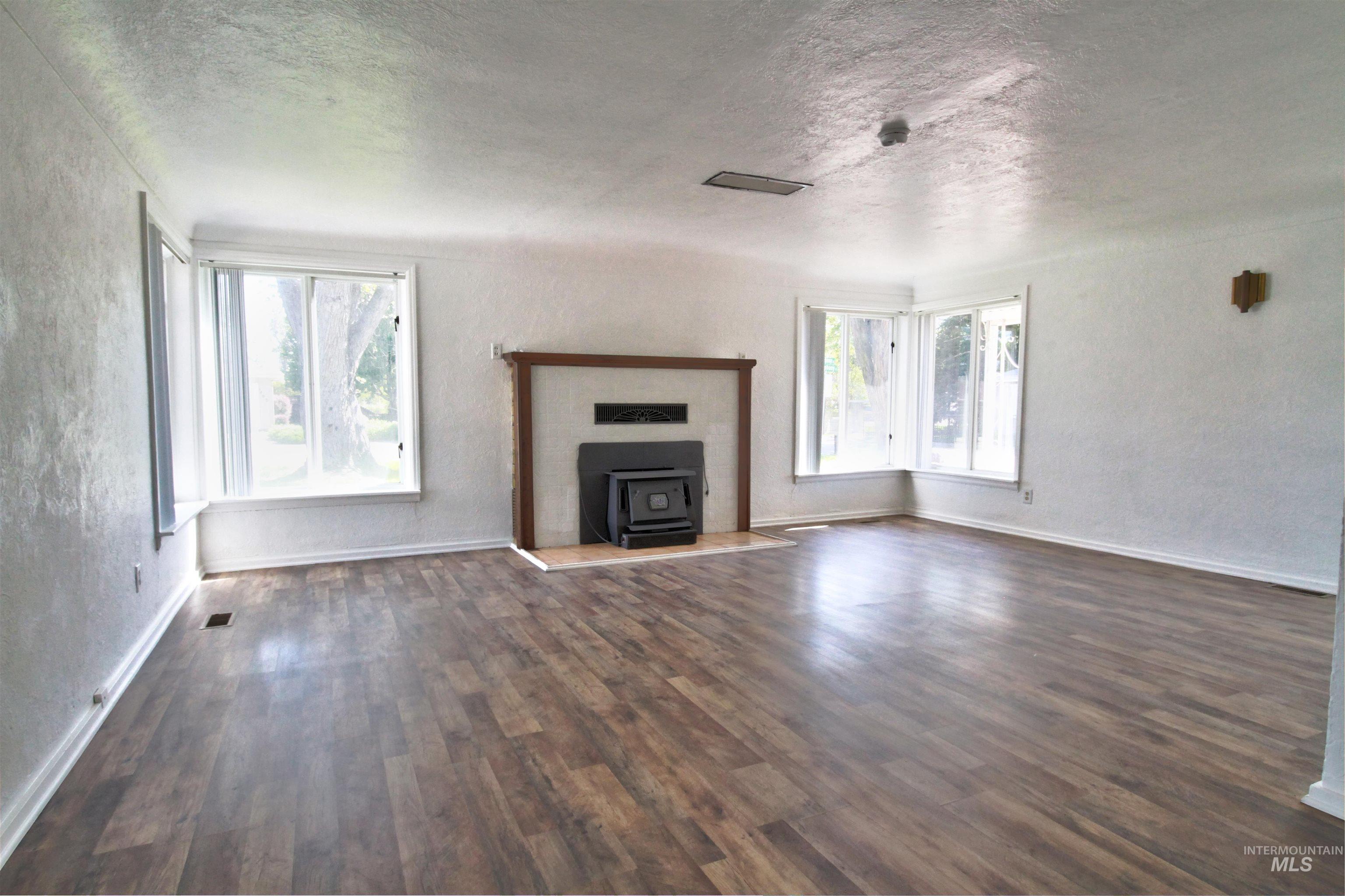 Unfurnished living room featuring a textured wall, a wood stove, a textured ceiling, and dark wood finished floors