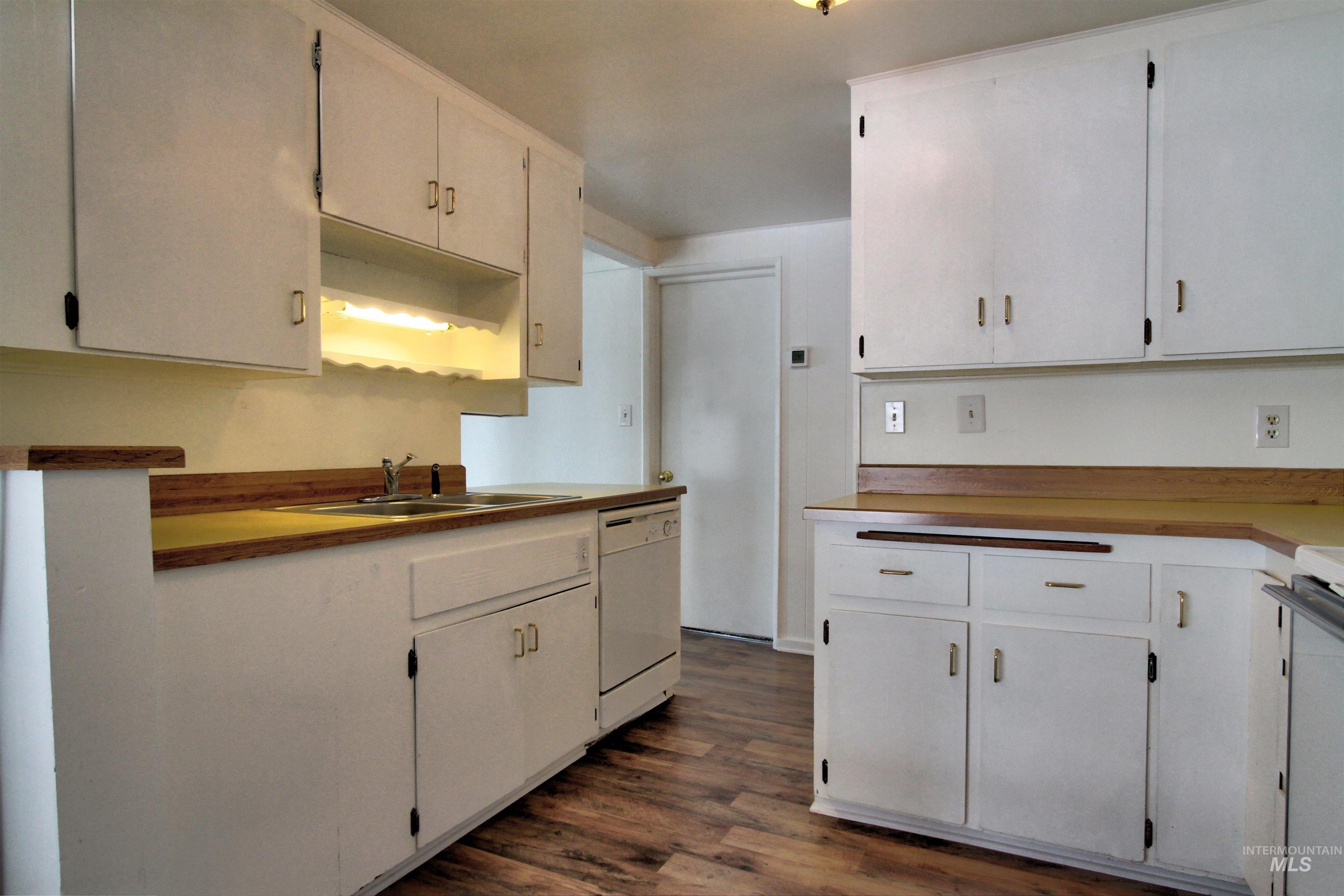 Kitchen featuring dark wood-type flooring, white dishwasher, light countertops, white cabinets, and stove
