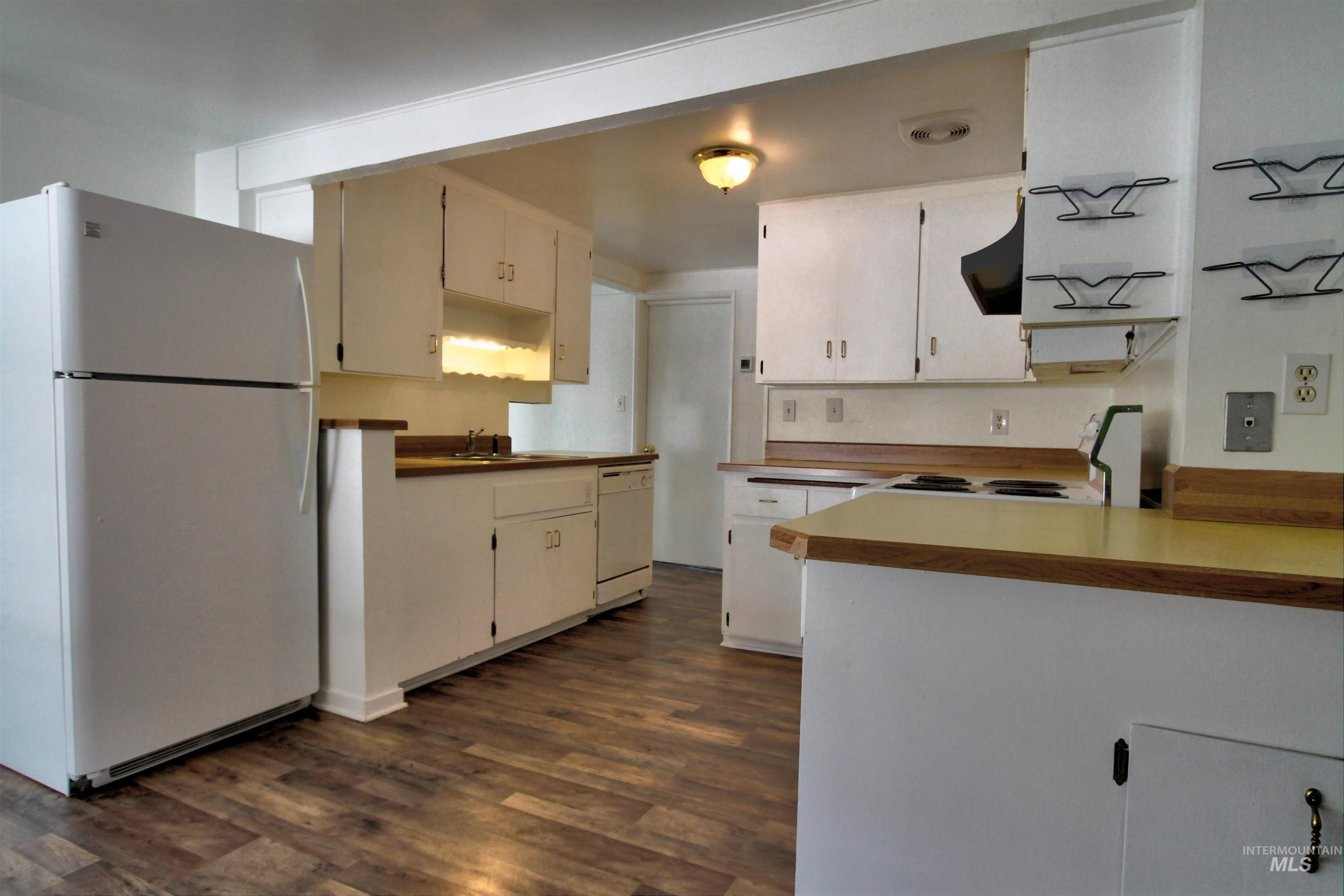 Kitchen featuring white appliances, dark wood-type flooring, white cabinetry, exhaust hood, and light countertops