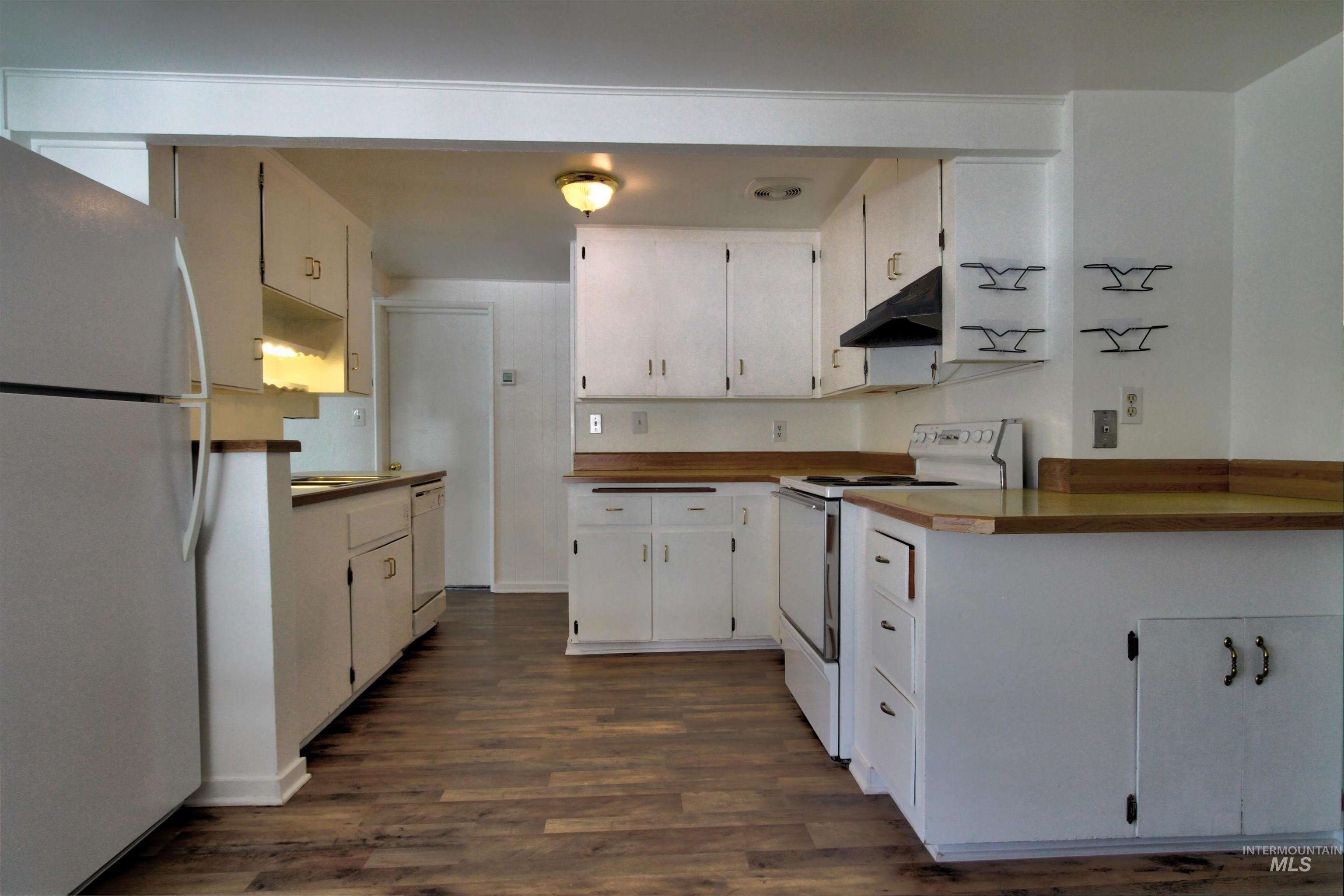 Kitchen with white appliances, dark wood-style flooring, under cabinet range hood, and white cabinets