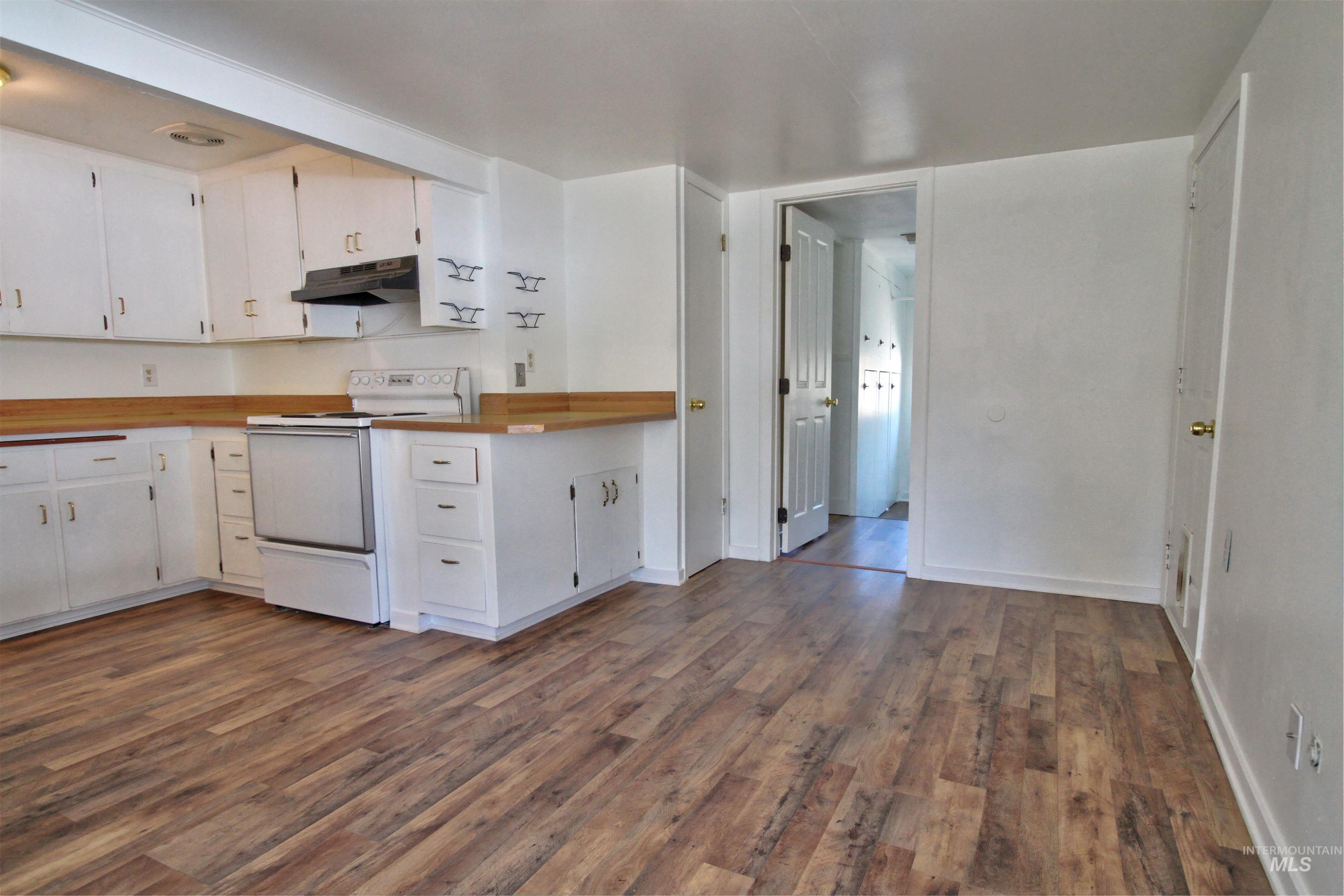 Kitchen with white electric stove, white cabinetry, under cabinet range hood, and dark wood-type flooring